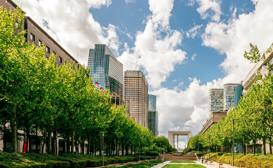 Straight parkway that blends urban buildings, lush green lawns, and blue skies