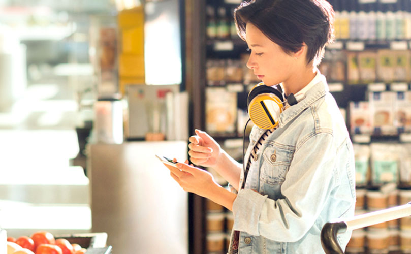 スマートフォンを見ながらスーパーで買い物をしている人の画像