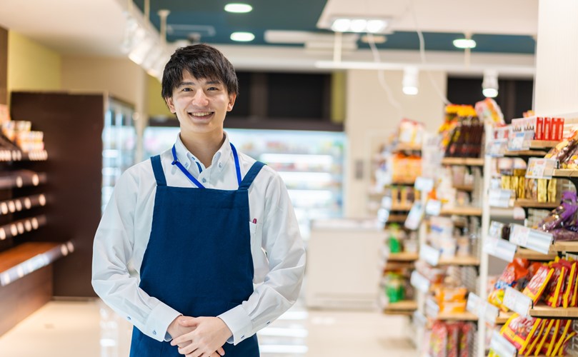 A happy supermarket employee with aisles full of groceries behind him