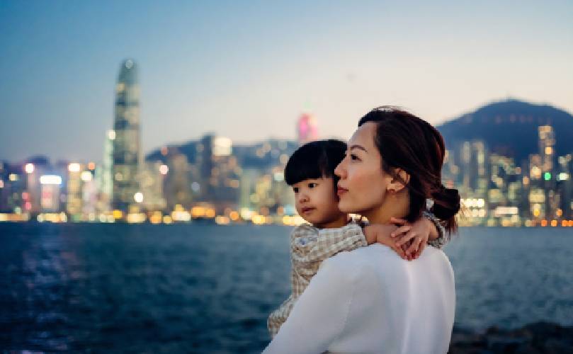 A woman with a child in her arms with the sea and a city in the background