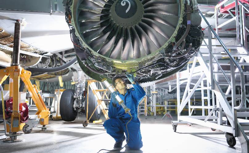 A man at an aircraft manufactory repairing an engine