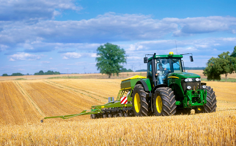 A tractor plowing a field of crops on a sunny day.