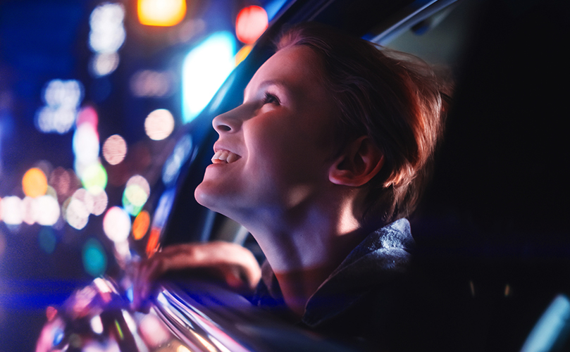 Image of a woman looking up and smiling from a car window at night