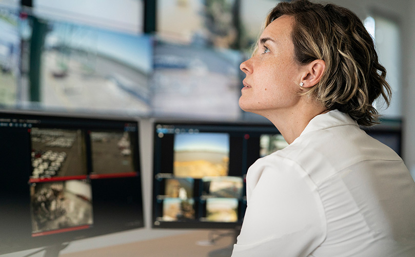 An adult female security guard sitting at a desk staring at a video wall