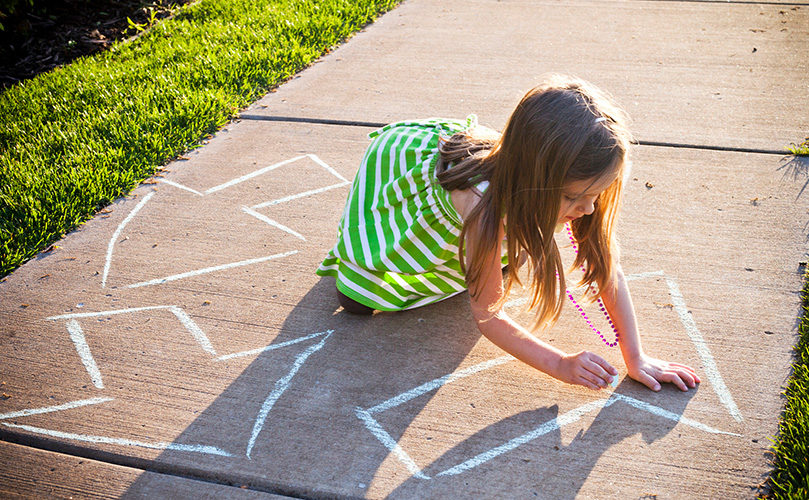A young girl writing a recycling symbol on the sidewalk