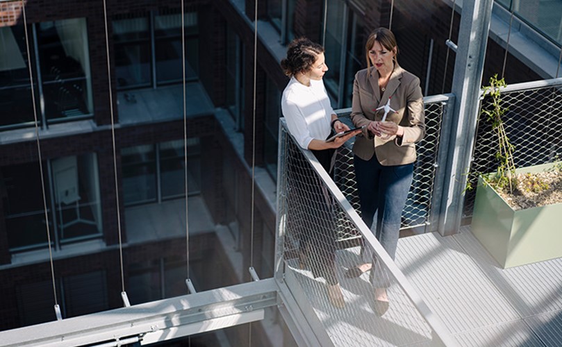 Two women having a conversation in a balcony next to a modern tall building