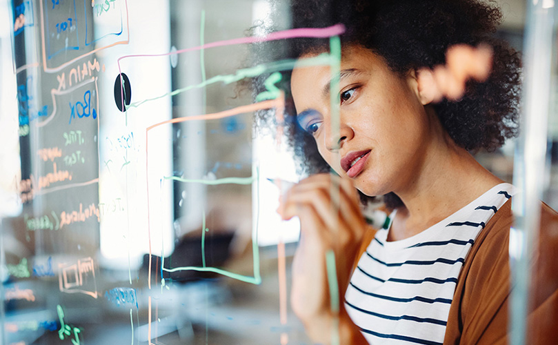 A female engineer thinking in front of a glass board in her office