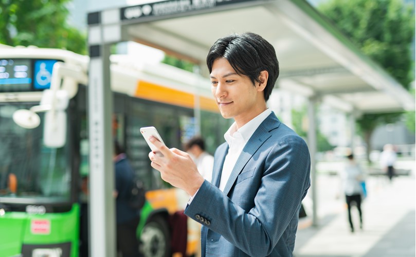 A man in a business suit watching his mobile phone at the bus station