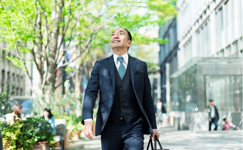  A person in a suit walking looking up to the sky, surrounded by trees.