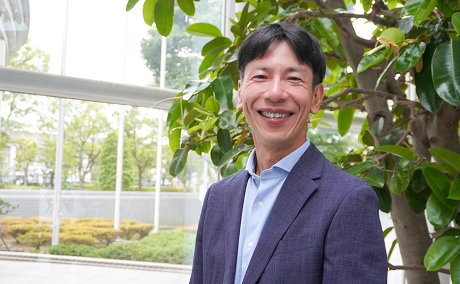 富士通株式会社 技術戦略本部 コミュニケーション戦略統括部 シニアディレクター 西川 博が緑の多いオフィスの前にて、笑顔で写る写真